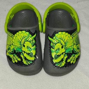 Crocs gray green dinosaur 
Dinosaurs glow in the dark 
Size 6 
Toddlers